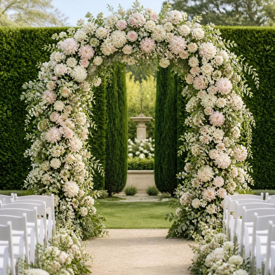 Arche de mariage entièrement fleurie de roses ivoire, pivoines et eucalyptus devant de grandes haies de jardin