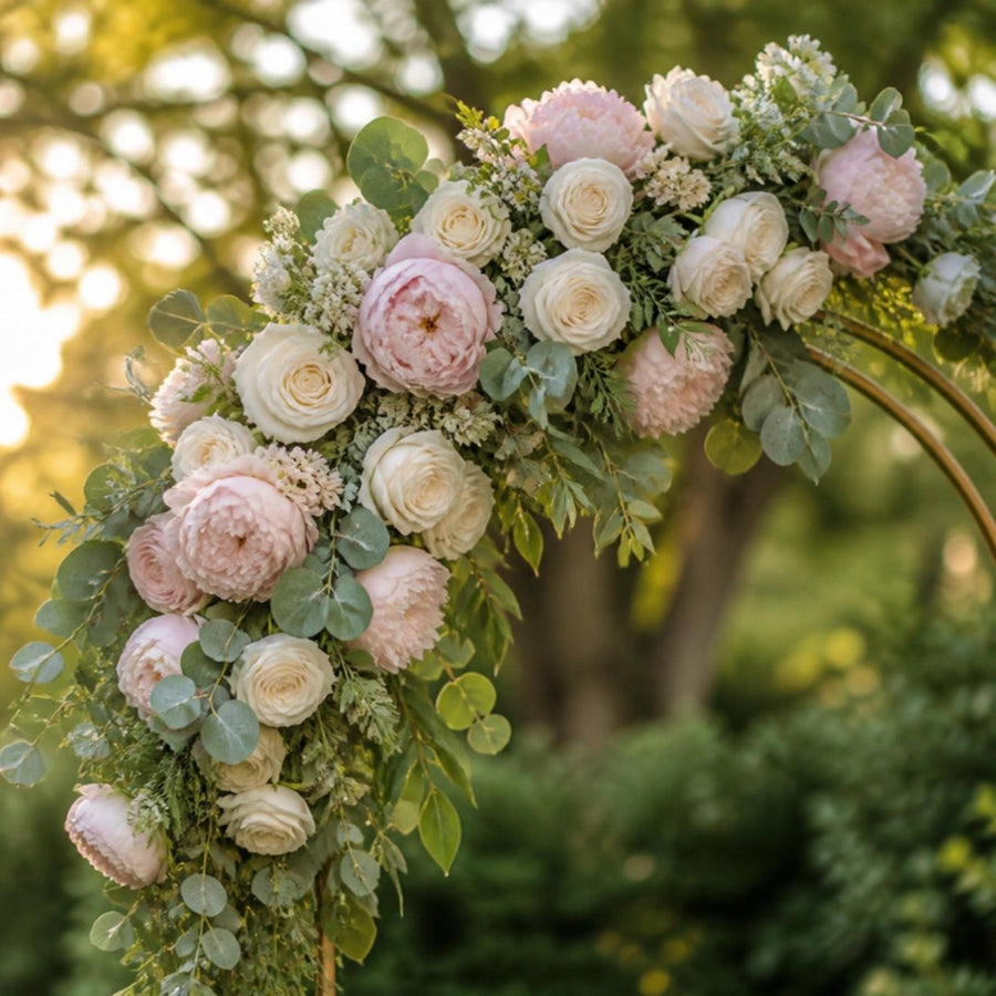 Gros plan sur une composition de roses ivoire, pivoines et eucalyptus fixée au coin d'une arche de mariage dorée
