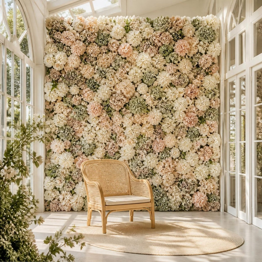 Mur de fleurs artificielles ivoire, rose poudré et sauge dans une orangerie lumineuse, avec fauteuil en cannage