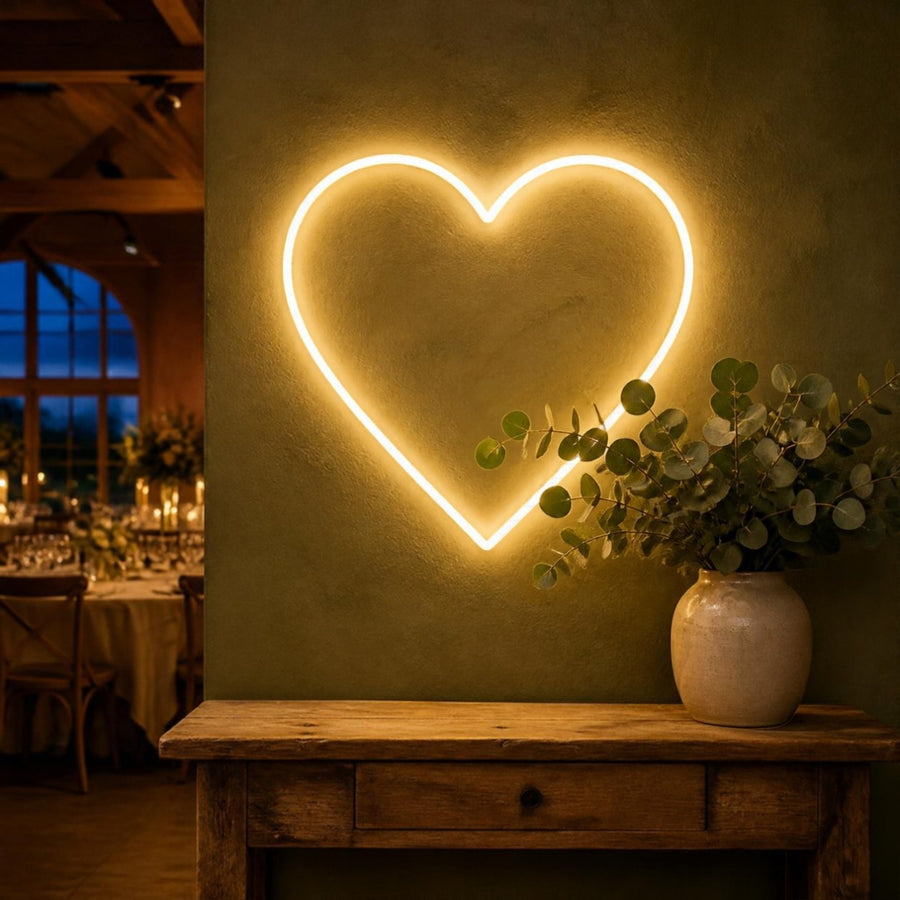 Néon mural en forme de coeur blanc chaud sur un mur vert sauge, au-dessus d'une console en bois, dans une salle de réception