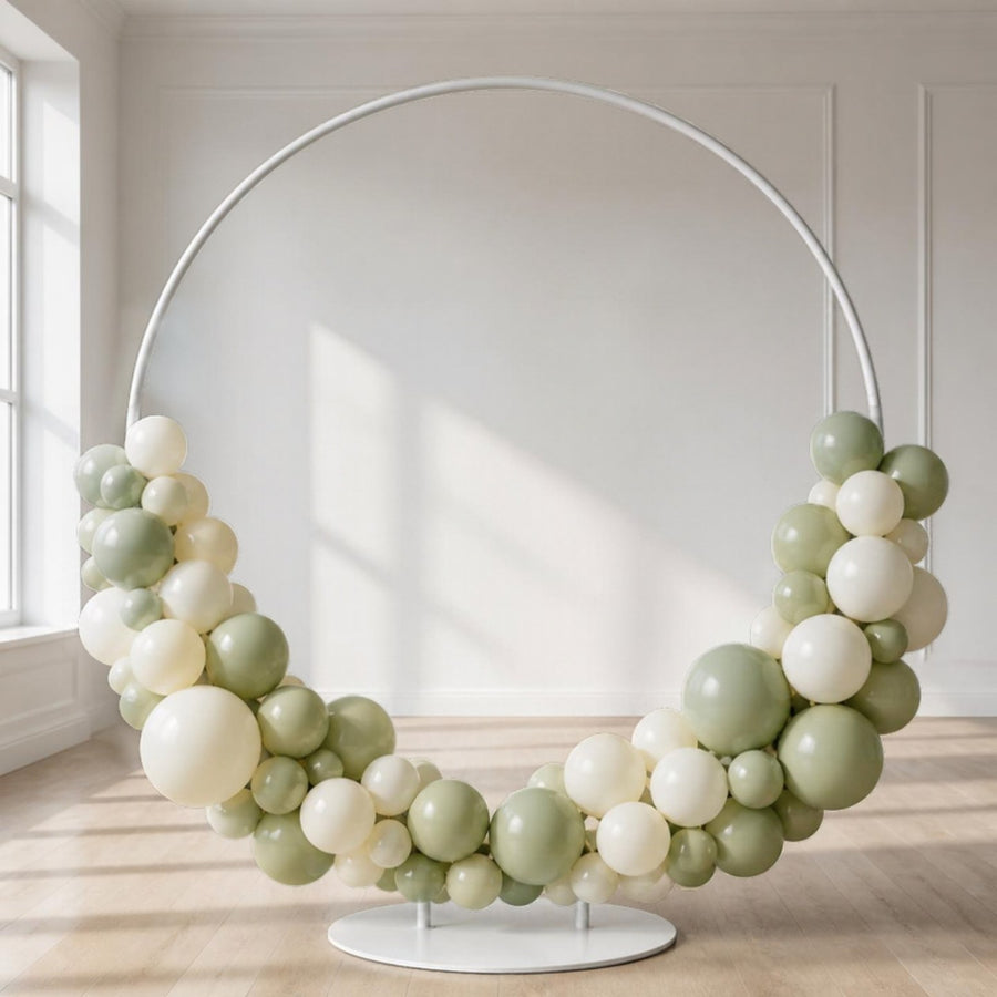 Structure d'arche de ballons en métal blanc, à moitié garnie de ballons sauge et ivoire, dans une salle claire